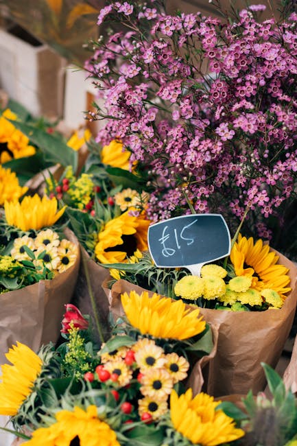 A vibrant display of freshly cut flowers at a local market, featuring yellow sunflowers with large, bright petals and dark centers, complemented by smaller yellow and white daisy-like blooms with gree